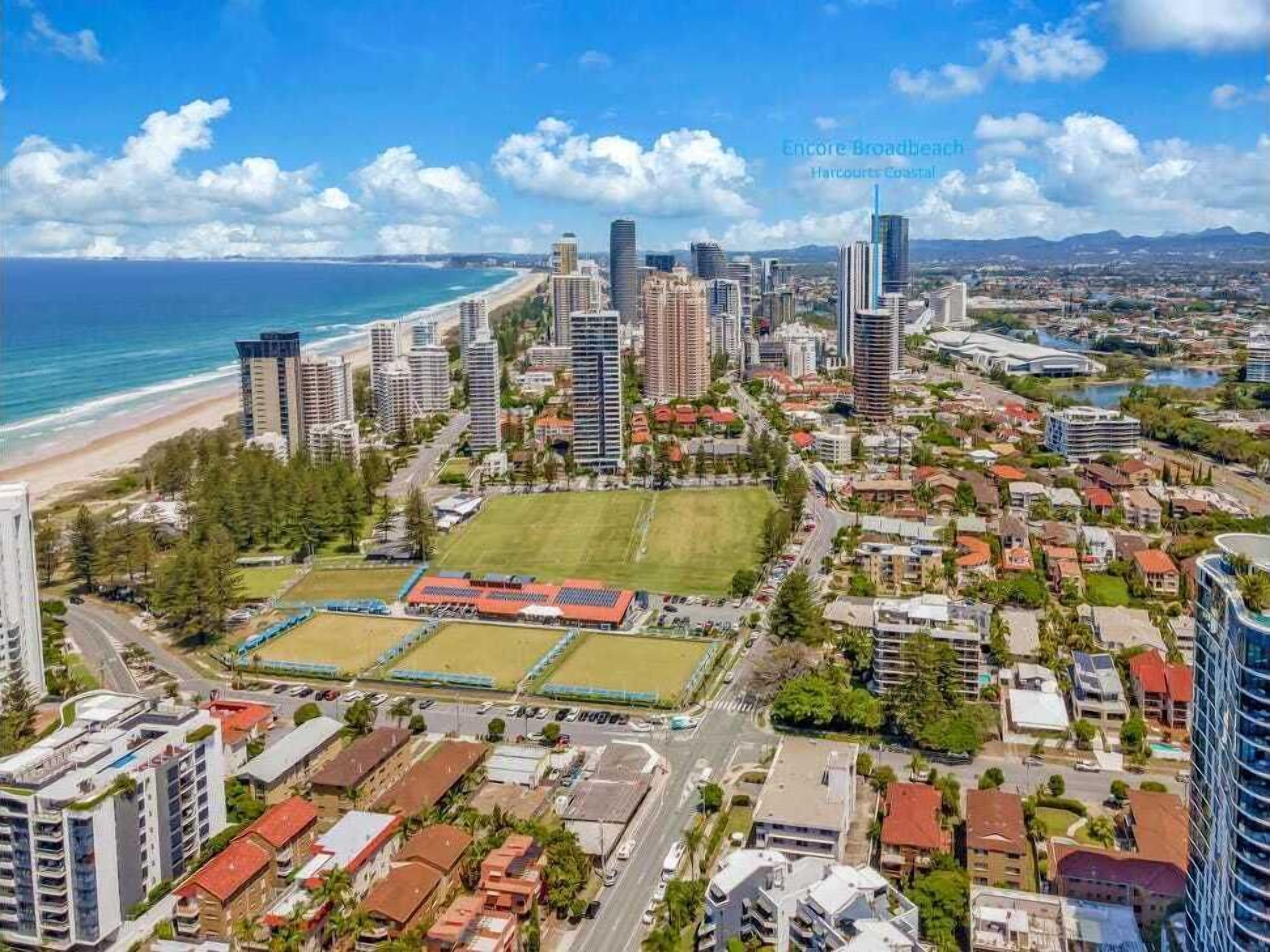 A coastal cityscape with high-rise buildings, a beach, and a sports field.