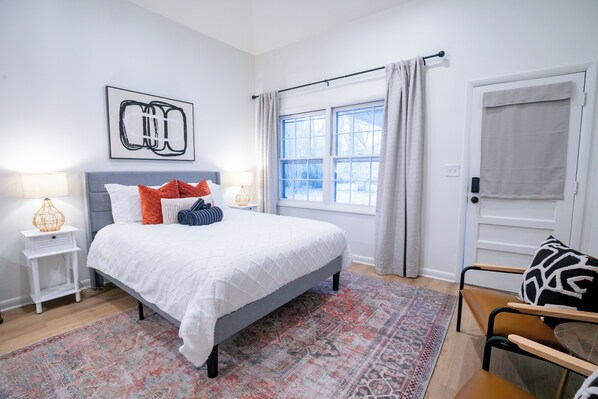A bedroom with a bed, nightstands, a chair, a window with curtains, and a door.