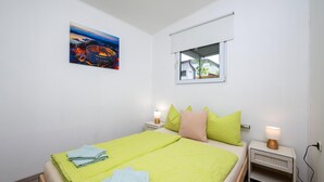 Une chambre à coucher avec un lit, des oreillers, une table de chevet avec une lampe, une fenêtre et un tableau au mur.
