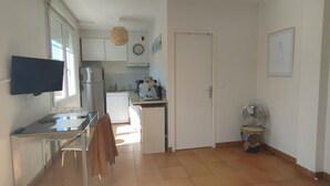 A compact kitchen with a refrigerator, stove, and microwave. There is a dining table with chairs and a TV mounted on the wall. - Le Petit Valentré Avec sa Superbe vue sur le Célèbre Pont et la Rivière Lot (Cahors)