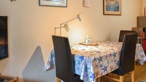 Ein Essbereich mit Tisch, der mit einer Tischdecke mit Sternfischmuster bedeckt ist, zwei Stühle, einer Lampe und gerahmten Bildern an der Wand.