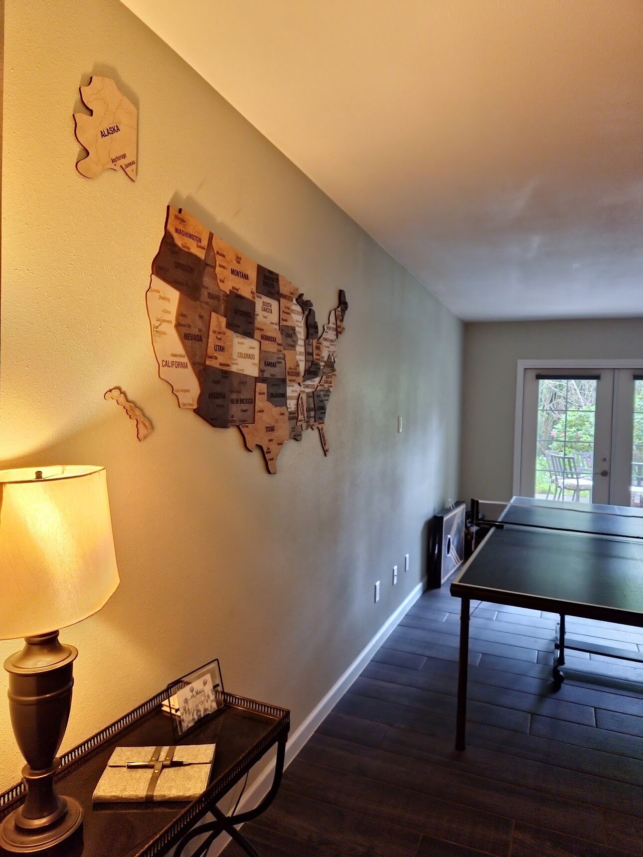 A room with a wall map of the United States, a table tennis table, a lamp, and a small table with a picture frame and a gift.