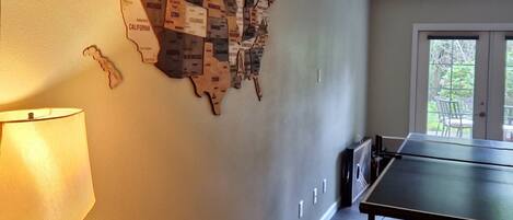 A room with a wall map of the United States, a table tennis table, a lamp, and a small table with a picture frame and a gift.
