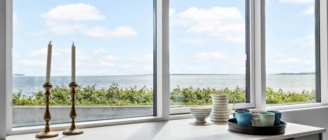 A kitchen with a large window overlooking a body of water, a white countertop, and a tray with blue and white mugs.