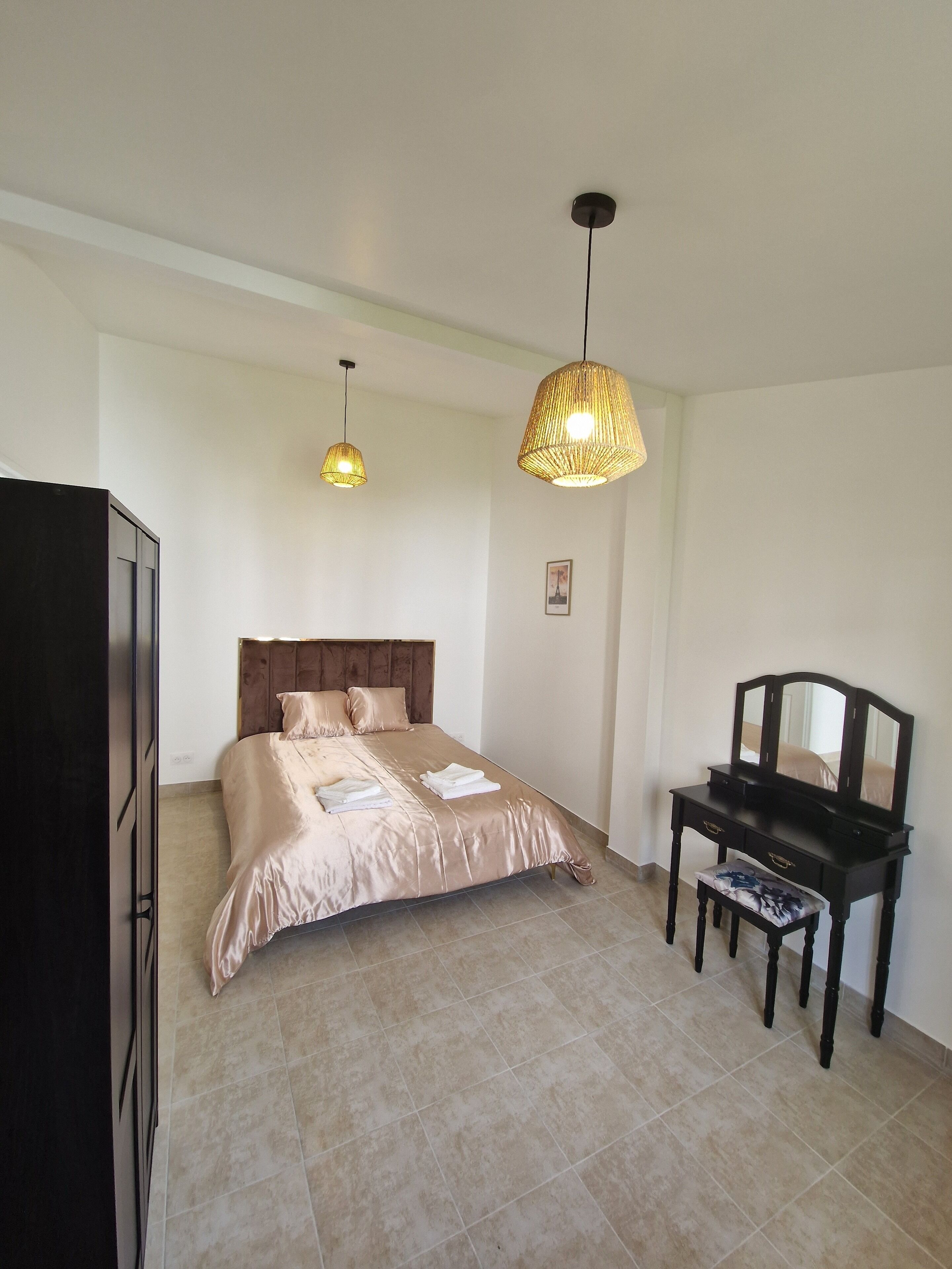 Ein Schlafzimmer mit einem Bett, einem Schminktisch, einem Sessel und zwei Pendelleuchten.