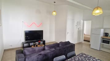 Una sala de estar moderna con un sofá, una mesa de comedor con mantel floral, un televisor de pantalla plana y lámparas colgantes.