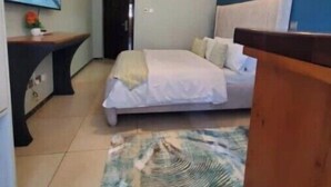 A bedroom with a bed, a desk, and a painting on the wall.