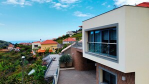 A modern building with large windows, a balcony, and a view of the sea. - Capelas House by LovelyStay (Campanario)