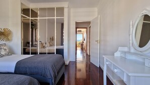 Une chambre avec un lit, une commode et un miroir. Un couloir mène à une autre pièce.