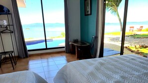 A hotel room with two beds, a desk, and a chair. There is a large window with a view of the beach and ocean. - Casa Celajes (Chomes)