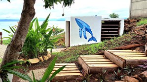 A wooden deck with a whale mural, surrounded by tropical plants and a view of the sea. - Casa Celajes (Chomes)