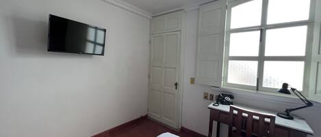 Habitación de hotel con cama, escritorio con silla, teléfono y televisor montado en la pared.