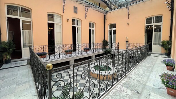 A courtyard with a checkered floor, a covered seating area with a railing, and potted plants. - Casa Chopo (Mexico City)