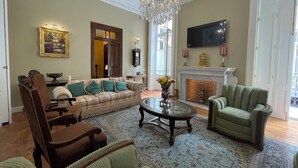 A living room with a sofa, armchairs, a coffee table, a fireplace, a chandelier, and a television. - Casa Chopo (Mexico City)