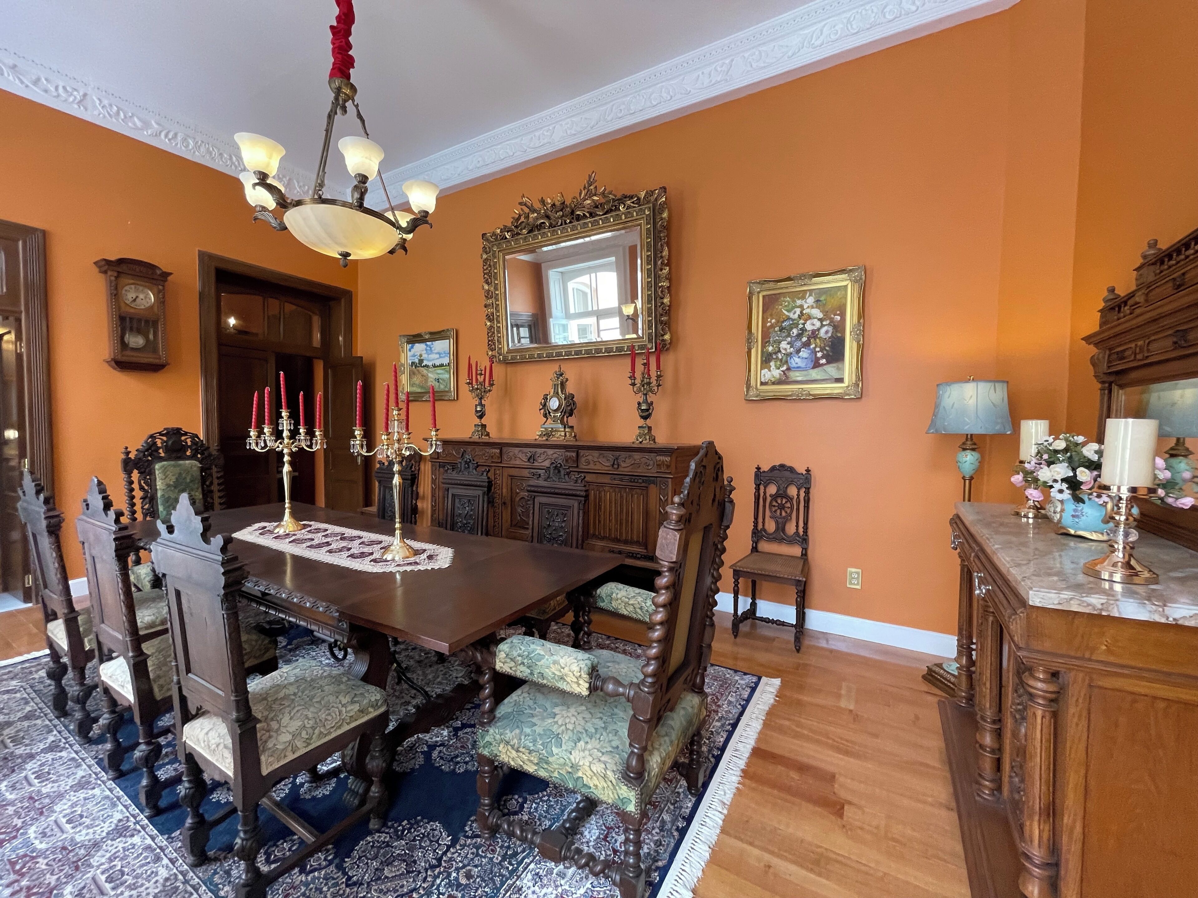 Un comedor formal con una gran mesa de madera, sillas ornamentadas, una araña y un espejo sobre la mesa.
