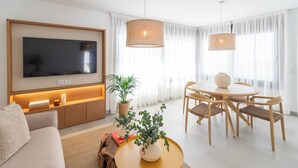 A modern living room with a flat-screen TV, wooden furniture, and a dining area with a round table and chairs. - Villa El Retiro de Torrox by Ruralidays (Málaga)