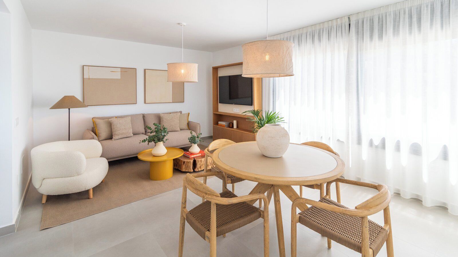A modern living room with a sofa, a round wooden dining table with chairs, a coffee table, and a TV.