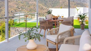 A terrace with wicker furniture, a vase with greenery, and a table with glasses and bread. - Villa El Retiro de Torrox by Ruralidays (Málaga)