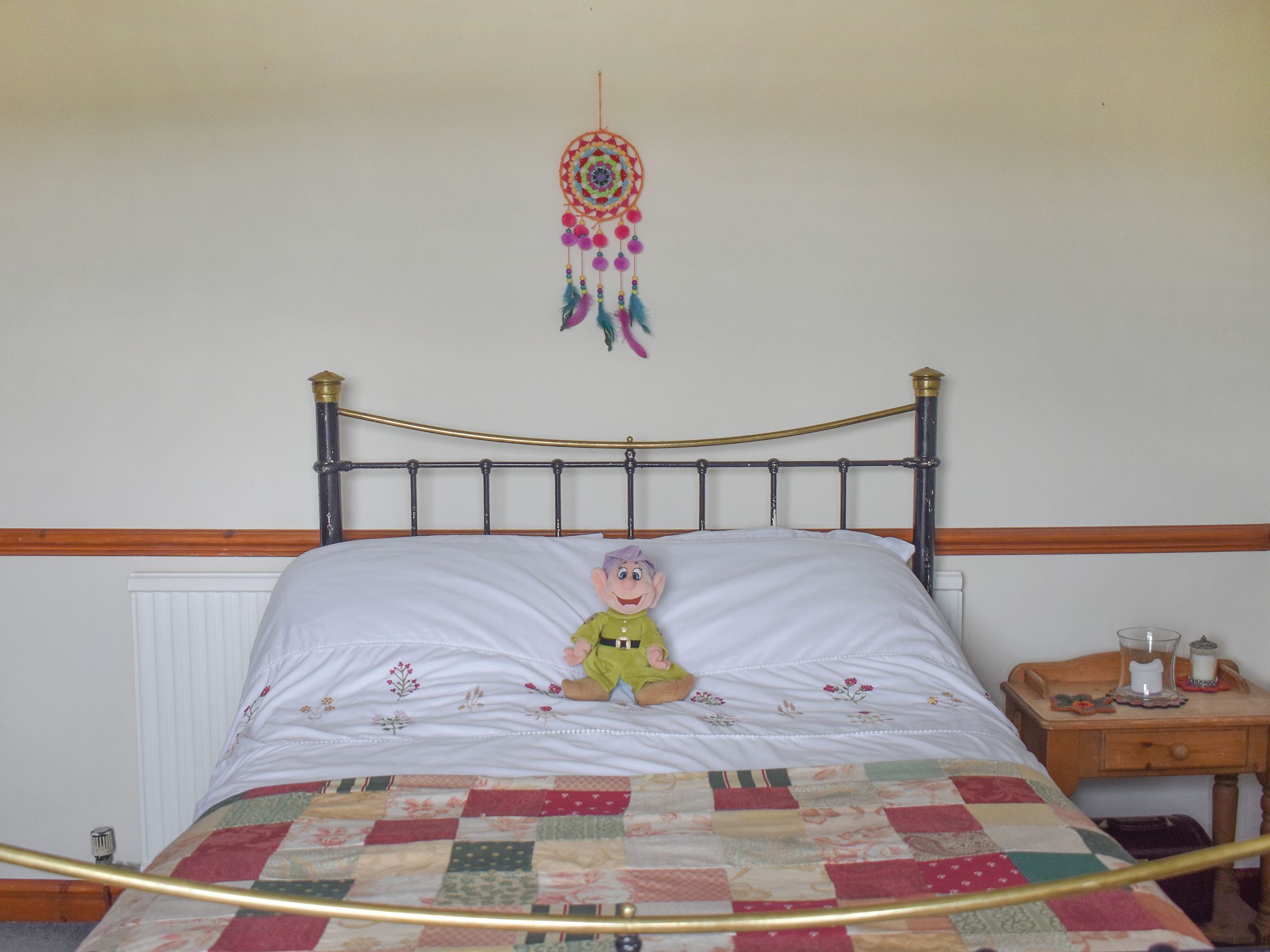 A bed with a quilt, a wooden bedside table with a glass, a candle, and a nightstand.