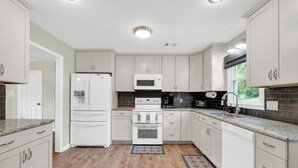 Una cocina moderna con gabinetes blancos, horno integrado, microondas y cafetera.