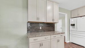 Una cocina con gabinetes de colores claros, encimera de granito y refrigerador de acero inoxidable.