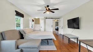 Un dormitorio moderno con cama, sofá, televisor y ventilador de techo.