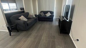 A modern living room with a dark grey sofa, a glass coffee table, and a flat-screen TV.