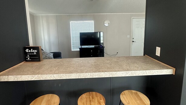 A kitchen area with a countertop, three stools, a black refrigerator, and a clock on the wall.