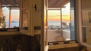 A room with a view of the sunset over the ocean, a potted plant, and a window with a view of parked cars. - Holiday Home 'Waterfront Masterpiece' with Sea View, Wi-Fi and Air Conditioning (Tinos)