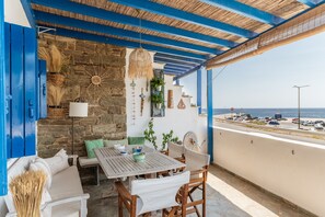 A covered outdoor seating area with a stone wall, a table, chairs, and a view of the sea. - Holiday Home 'Waterfront Masterpiece' with Sea View, Wi-Fi and Air Conditioning (Tinos)