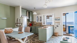 A kitchen with a dining area, stone flooring, and a view through an open door. - Holiday Home 'Waterfront Masterpiece' with Sea View, Wi-Fi and Air Conditioning (Tinos)