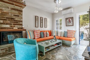 A living room with a brick fireplace, a sofa with patterned cushions, a coffee table, and a stone floor.
