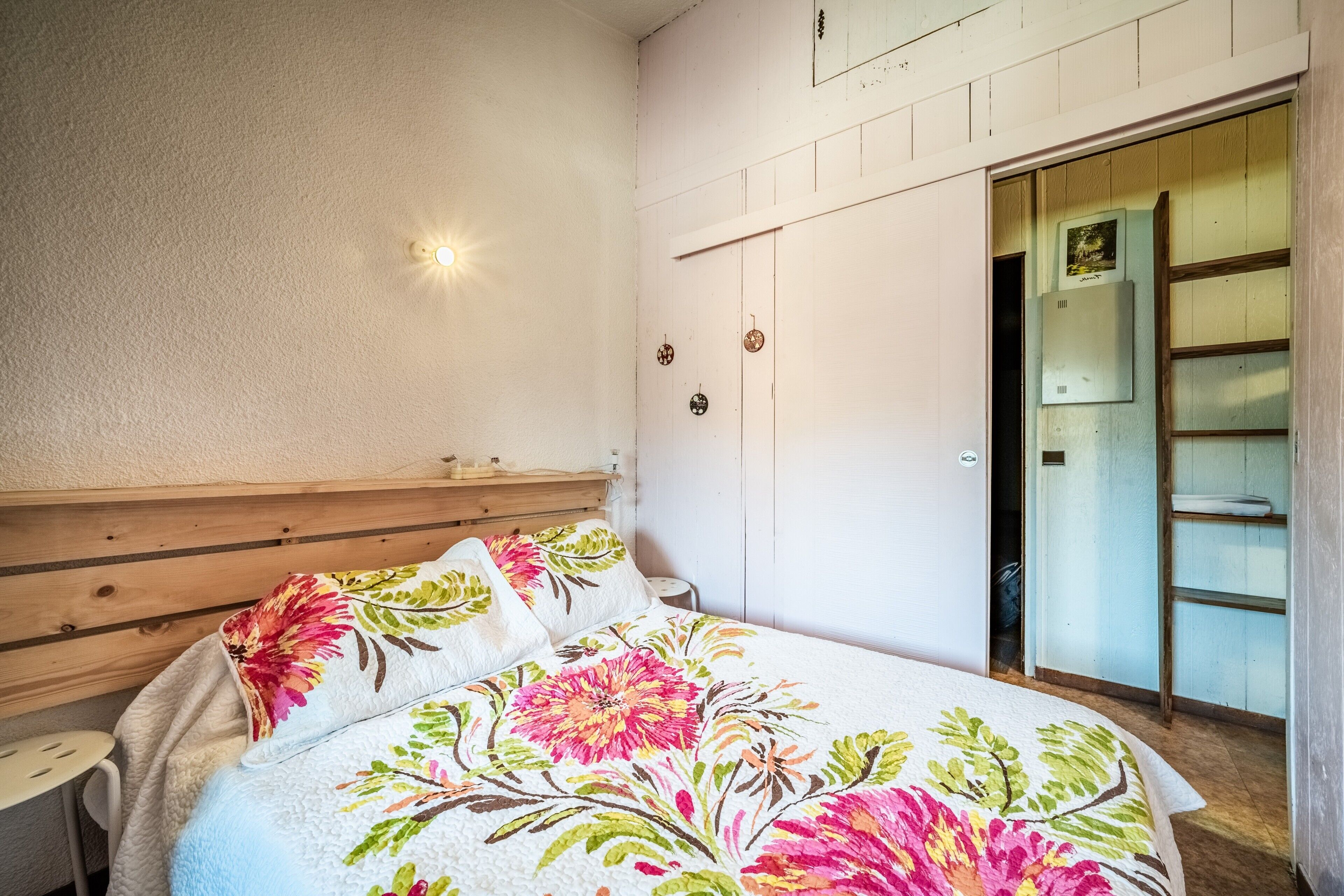 Une chambre à coucher avec une tête de lit en bois, une couvre-lit à motifs floraux, une table de chevet et une armoire avec un miroir.