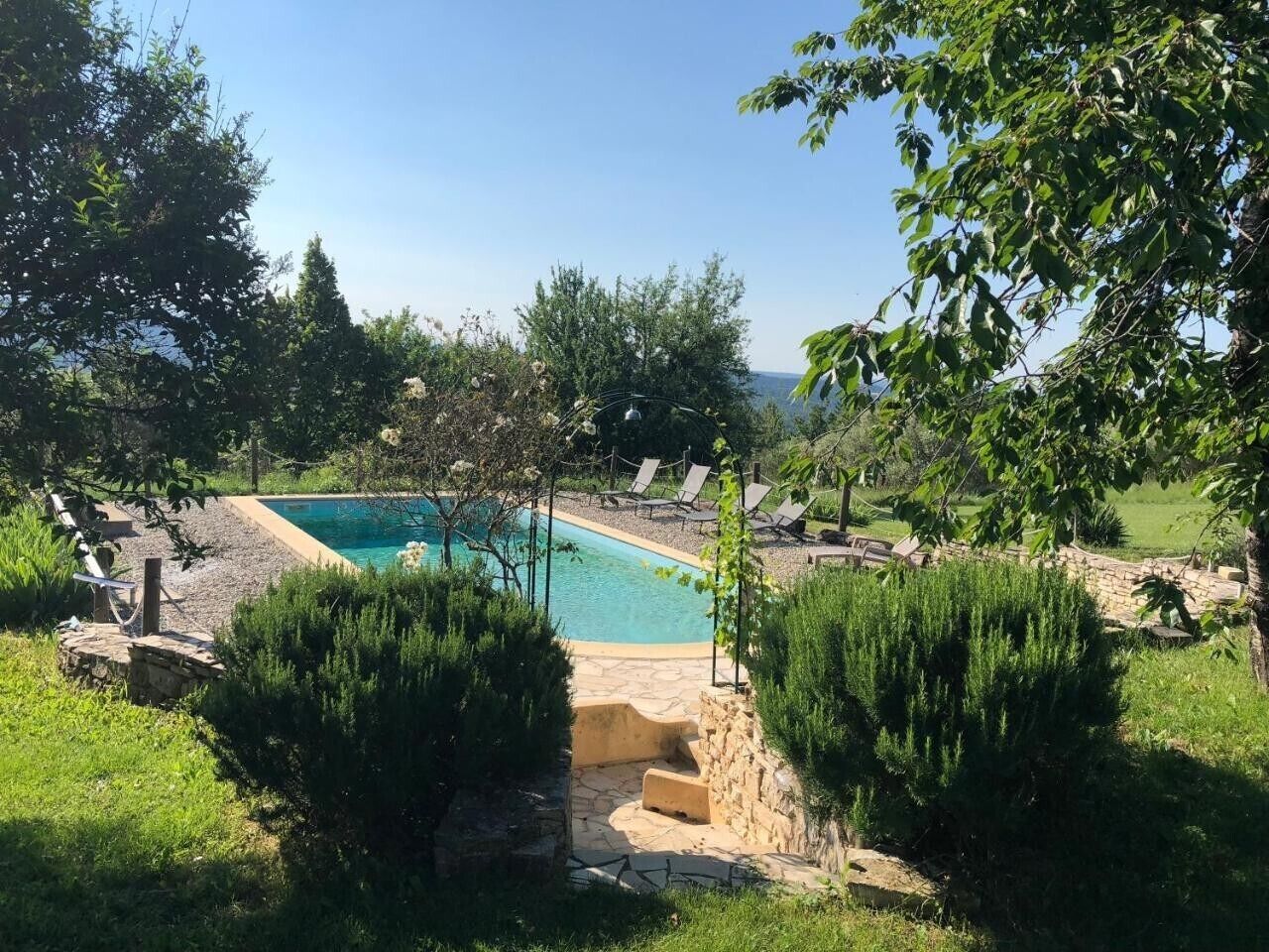 Une piscine entourée de chaises longues, de verdure et de murs en pierre.