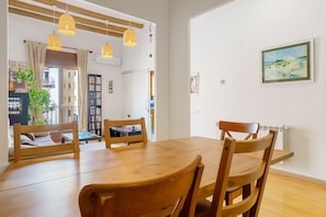 Een eetruimte met een houten tafel en stoelen, hanglampen en een lijstwerk schilderij aan de muur.