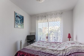 A bedroom with a bed, a television, a radiator, and a window with a curtain.