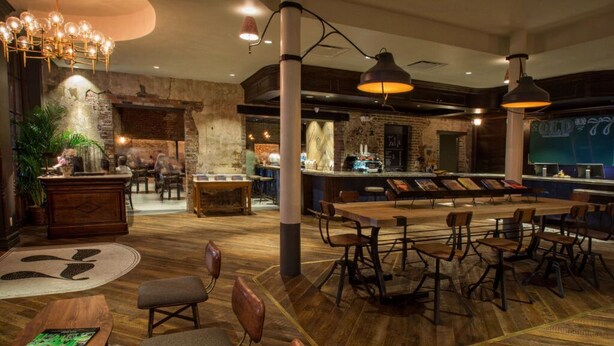 A spacious bar area with high stools and a long counter, surrounded by wooden tables and chairs.