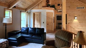 Una habitación acogedora con techo de madera, un sofá de cuero negro, un sillón verde y una lámpara.