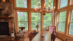 Un comedor espacioso con una larga mesa de madera, rodeada de sillas, ventanas amplias y una chimenea de piedra.