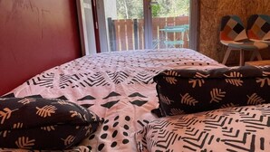 A bedroom with a bed, pillows, a wooden wall, a balcony, and a view of trees.