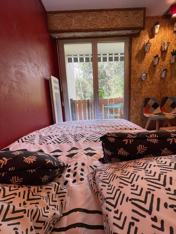 A bedroom with a bed, pillows, a wooden wall, a balcony, and a view of trees. - Apartment "Le Pélican" with Private Terrace, Balcony and Wi-Fi (Saint-Georges-de-Didonne)