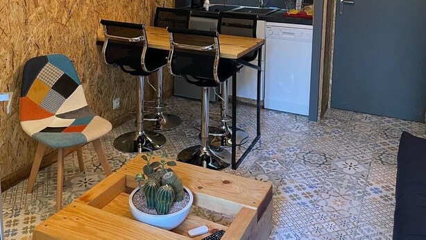 A compact kitchen with a dining area, a bar stool, a coffee machine, and a potted plant.