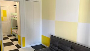 Una habitación con piso a cuadros, un sofá de cuero negro, una mesa redonda amarilla y un armario blanco.
