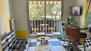 Una habitación con suelo a cuadros, un sofá, una mesita, una silla, un televisor y vistas al exterior por una ventana.