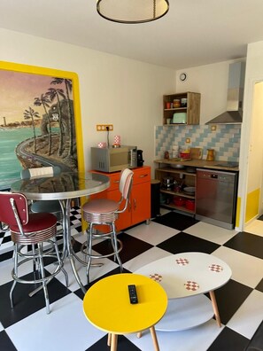 Een compacte keuken met een eethoek, een schilderij aan de muur en een zwart-wit geruit vloerkleed.
