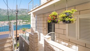 Un balcon orné de jardinières suspendues, une vue sur une ville côtière et un ciel dégagé.