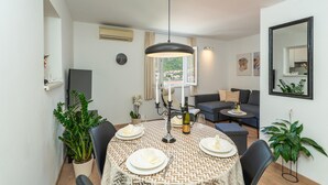 Un coin repas avec une table ronde dressée pour quatre personnes, un luminaire suspendu moderne et un canapé en arrière-plan.