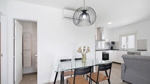 A modern kitchen with white cabinets, a grey sofa, and a glass dining table with chairs.