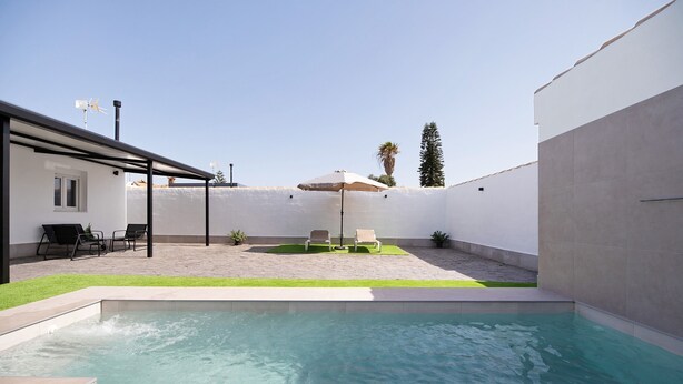 A swimming pool with a patio area, outdoor seating, and a covered structure.