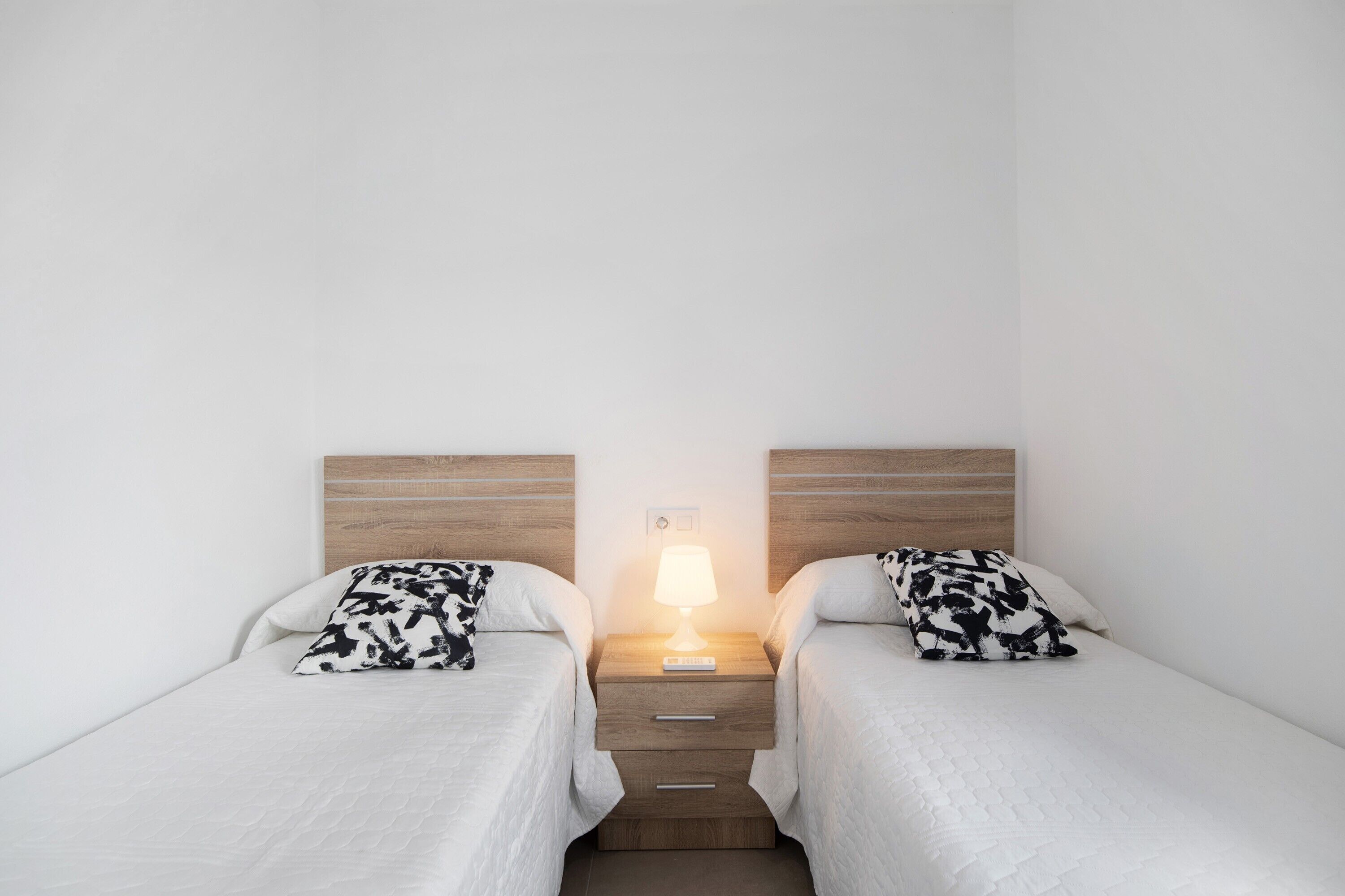 A twin room with two single beds, a nightstand with a lamp, and a wooden headboard.
